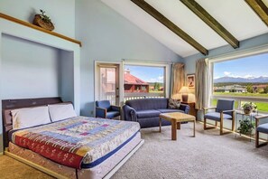 Ein Schlafzimmer mit Bett, Sofa, Couchtisch und Blick auf ein Haus und Berge.