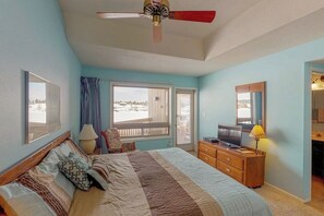 Un dormitorio con cama, televisor, cómoda, ventilador de techo y ventana con vistas.