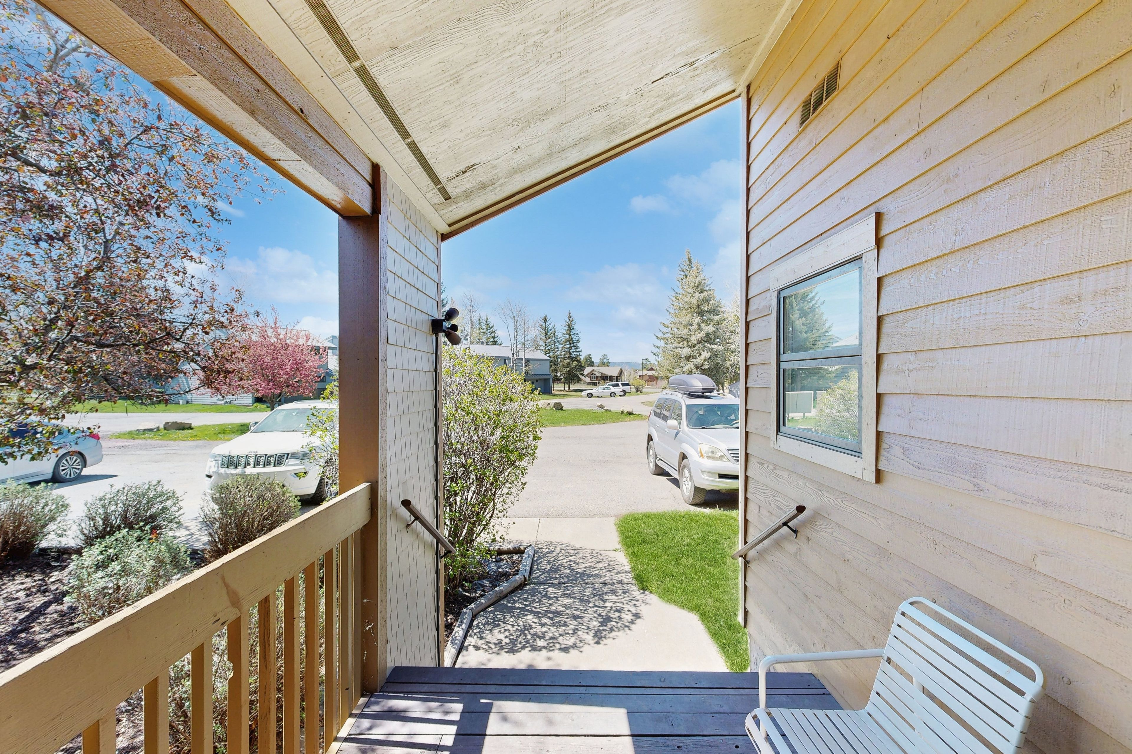 A wooden building with a porch, a bench, and a view of a driveway with parked cars.