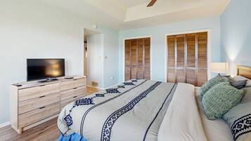 A bedroom with a bed, a television on a wooden dresser, a ceiling fan, and wooden shutters on the windows.