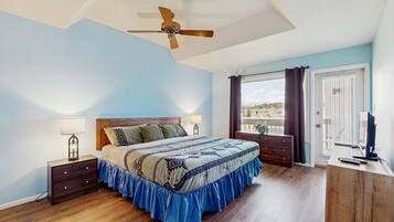 A bedroom with a bed, bedside tables, a ceiling fan, a window with curtains, and a desk with a computer.