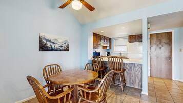 A dining area with a round wooden table and chairs, a ceiling fan, and a kitchen in the background.
