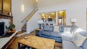 Un salon avec une cheminée, un canapé, une table basse et un escalier menant à la cuisine.