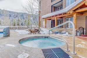 A hot tub with a wooden deck, a stone wall, and a view of snow-covered trees. - Newly renovated mountain escape with pool, hot tub, WiFi & easy slope access (Keystone)