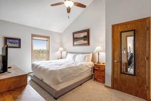 A bedroom with a bed, two bedside tables with lamps, a ceiling fan, a wooden door, and a window with a view. - Ski-in/ski-out home with pool, hot tub, sauna, washer/dryer, & private balcony (Keystone)