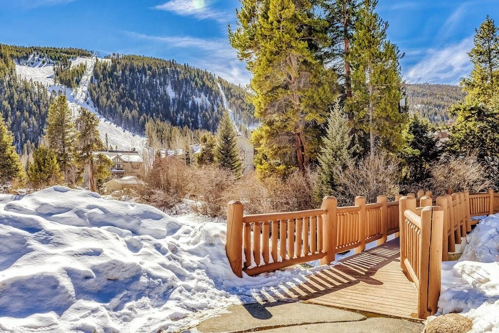 Eine Holzbrücke über Schnee, umgeben von Bäumen und einem Berg.