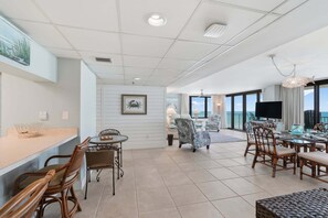 A spacious living area with a dining table, chairs, a TV, and a balcony with a view. - Watercrest 603 - Free Beach Chairs! (Panama City)