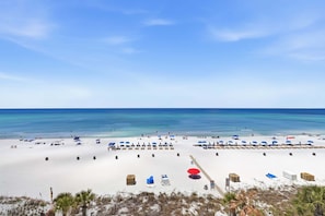 A beach with rows of umbrellas and sun loungers, a clear sky, and the ocean in the background. - Watercrest 603 - Free Beach Chairs! (Panama City)