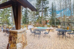 An outdoor patio with stone flooring, metal tables and chairs, a hot tub, and a wooden pergola structure. - Gorgeous mountain condo with fireplace, scenic balcony, walk-in shower, & W/D (Keystone)