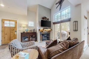 A spacious living area with a fireplace, a television mounted on the wall, and a large window providing natural light. - Gorgeous mountain condo with fireplace, scenic balcony, walk-in shower, & W/D (Keystone)