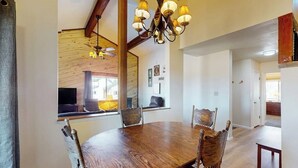 Een eethoek met een houten tafel en stoelen, een kroonluchter en een groot raam met uitzicht.