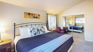 Een slaapkamer met een bed, een nachtkastje, een stoel, een bureau, een spiegel en een deur naar een andere kamer.