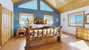 Ein Schlafzimmer mit schrägverdeckter Decke, Holzmöbeln und großen Fenstern.