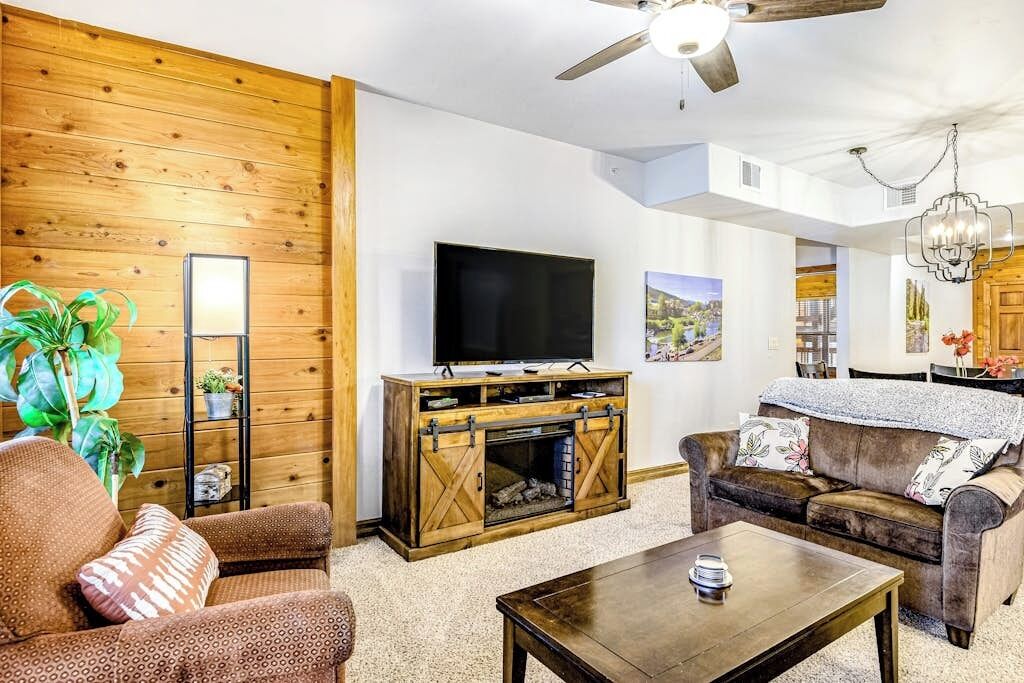 A living room with a TV, wooden wall paneling, a sofa, a coffee table, and a ceiling fan.