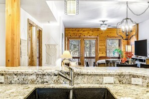 A kitchen with granite countertops, a sink, wooden walls, a chandelier, and a dining area with a TV. - Convenient dog-friendly, course-front condo with washer/dryer - near hot springs (Pagosa Springs)