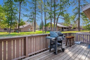 Eine Terrasse mit Grill und Hockern, umgeben von Bäumen und Häusern.