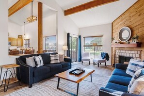 A spacious living area with a fireplace, a sofa, a coffee table, and a dining area with wooden cabinets and a hanging light fixture. - Family-Friendly Condo w/ High-Speed WiFi, Washer/Dryer, & Central AC (Pagosa Springs)