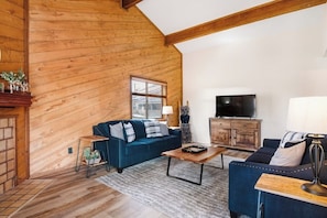 Ein gemütliches Wohnzimmer mit Holzwänden, einem blauen Sofa, einem Couchtisch, einem Fernseher und einem Kamin.