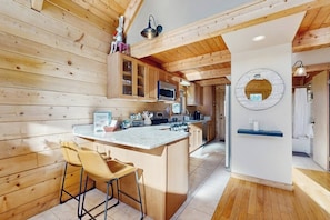 A wooden cabin interior with a kitchen island, bar stools, and a round mirror on the wall. - Cozy modern cabin with private hot tub, grill, deck, balcony, & W/D (Pagosa Springs)