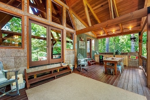 A wooden deck with a dining area, rocking chairs, and a view of the surrounding forest.