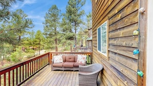 A wooden deck with a sofa and wicker chair, surrounded by trees. - Comfortable home with large deck, fully stocked kitchen, wifi & great location (Pagosa Springs)