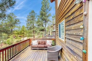 A wooden deck with a sofa and wicker chair, surrounded by trees.