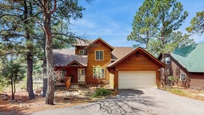 A two-story log cabin with a garage, surrounded by pine trees. - Comfortable home with large deck, fully stocked kitchen, wifi & great location (Pagosa Springs)