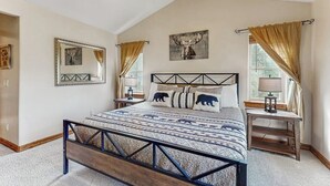 A bedroom with a bed, a headboard, a bedside table, a lamp, a mirror, and a window with curtains. - Comfortable home with large deck, fully stocked kitchen, wifi & great location (Pagosa Springs)