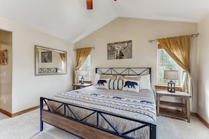 A bedroom with a bed, a headboard, a bedside table, a lamp, a mirror, and a window with curtains.