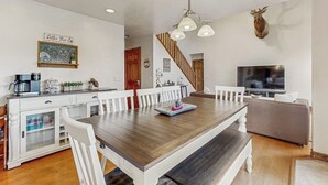 A dining area with a wooden table, white chairs, a coffee station, a television, and a mounted deer head. - Comfortable home with large deck, fully stocked kitchen, wifi & great location (Pagosa Springs)