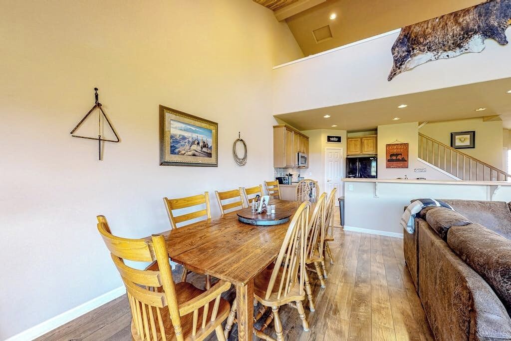 Un coin repas avec une table et des chaises en bois, une cuisine à l’arrière-plan et un escalier menant à un niveau supérieur.