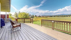 Une terrasse en bois avec des meubles d’extérieur, une vue sur un champ verdoyant et des montagnes au loin.