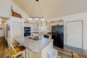 A kitchen with a central island, wooden chairs, a black refrigerator, and a hanging light fixture. - Log Home with Mountain Views, Firepit & Gas Fireplace - Quick Drive to Skiing (Tabernash)
