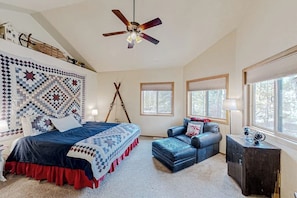 A bedroom with a bed, a blue sofa, a wooden cabinet, and a ceiling fan. - Log Home with Mountain Views, Firepit & Gas Fireplace - Quick Drive to Skiing (Tabernash)
