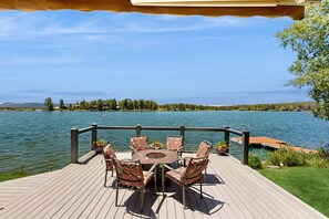 A wooden deck with a round table and chairs, overlooking a lake with a distant shoreline. - Stunning lake house with dock, firepit, grill, canoes, & mountain views (Pagosa Springs)
