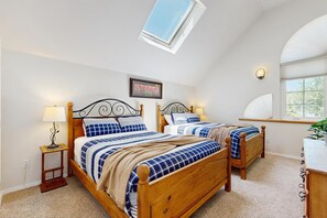 A bedroom with two wooden beds, a skylight, a framed picture, and a bedside table with a lamp. - Stunning lake house with dock, firepit, grill, canoes, & mountain views (Pagosa Springs)