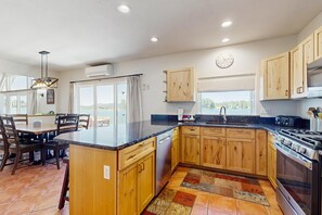A kitchen with wooden cabinets, a black countertop, a built-in oven, and a dining area with chairs and a table. - Stunning lake house with dock, firepit, grill, canoes, & mountain views (Pagosa Springs)