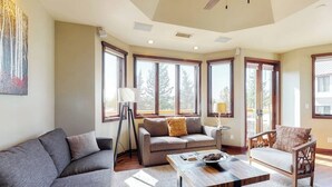 A living room with a sofa, a coffee table, and a chair. There are large windows and a ceiling fan. - Meadows Clarion 2, Mountainview condo w/ three fireplaces, shared pool and hot tub & winter shuttle (Steamboat Springs)