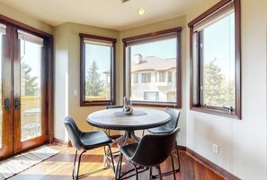 Ein Eckzimmer mit rundem Tisch und vier Stühlen, großen Fenstern und Blick auf ein Gebäude.