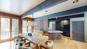 Cozinha moderna com armários de madeira, uma mesa de jantar com cadeiras e vista para o exterior através de grandes janelas.