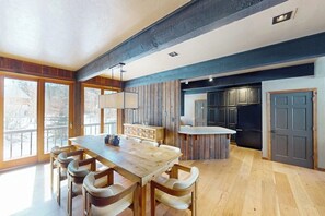 A modern kitchen with wooden cabinets, a dining table with chairs, and a view of the outdoors through large windows. - Charming mountain home with hot tub, views, and cozy fireplace (Vail)