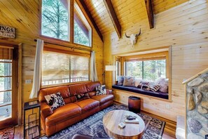 Ein Interieur einer Holzhütte mit Ledersofa, rundem Couchtisch und Kamin aus Stein.