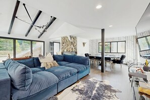 A modern living room with a blue sectional sofa, a dining area, and a stone accent wall. - Charming Vail House with Cozy Fireplace, Jetted Tub & Scenic Mountain Views (Vail)