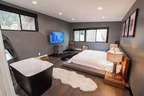 A modern bedroom with a large window, a bathtub, a bed, and a television. - Charming Vail House with Cozy Fireplace, Jetted Tub & Scenic Mountain Views (Vail)