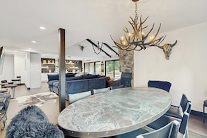 A modern dining area with a round table, blue upholstered seating, and a unique antler chandelier. - Charming Vail House with Cozy Fireplace, Jetted Tub & Scenic Mountain Views (Vail)