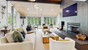Amplia sala de estar con techo alto, ventanas grandes, chimenea y televisor de pantalla plana montado en la pared.