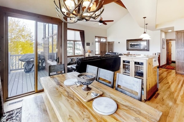 A spacious kitchen with a large island, a dining area with a wooden table, and a sliding glass door leading to an outdoor deck. - Attractive & Spacious Countryside Home w/Firepit, Private W/D, Free WiFi, Patio (Granby)