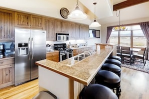 A kitchen with a central island, stainless steel appliances, wooden cabinets, and a view through large windows. - Attractive & Spacious Countryside Home w/Firepit, Private W/D, Free WiFi, Patio (Granby)