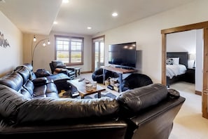 A modern living room with a leather sofa, a flat-screen TV, and a large window. - Attractive & Spacious Countryside Home w/Firepit, Private W/D, Free WiFi, Patio (Granby)