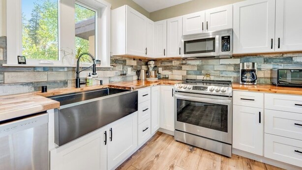 A modern kitchen with white cabinets, a stainless steel sink, a microwave, an oven, and a coffee maker. - Two-story dog-friendly getaway with WiFi, wood-burning fireplace, & washer/dryer (Fraser)